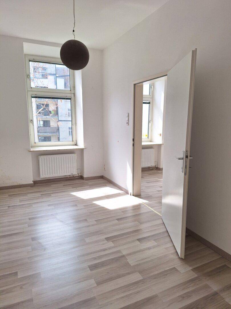 Helles Zimmer mit Laminatboden und viel Tageslicht durch die Fenster.