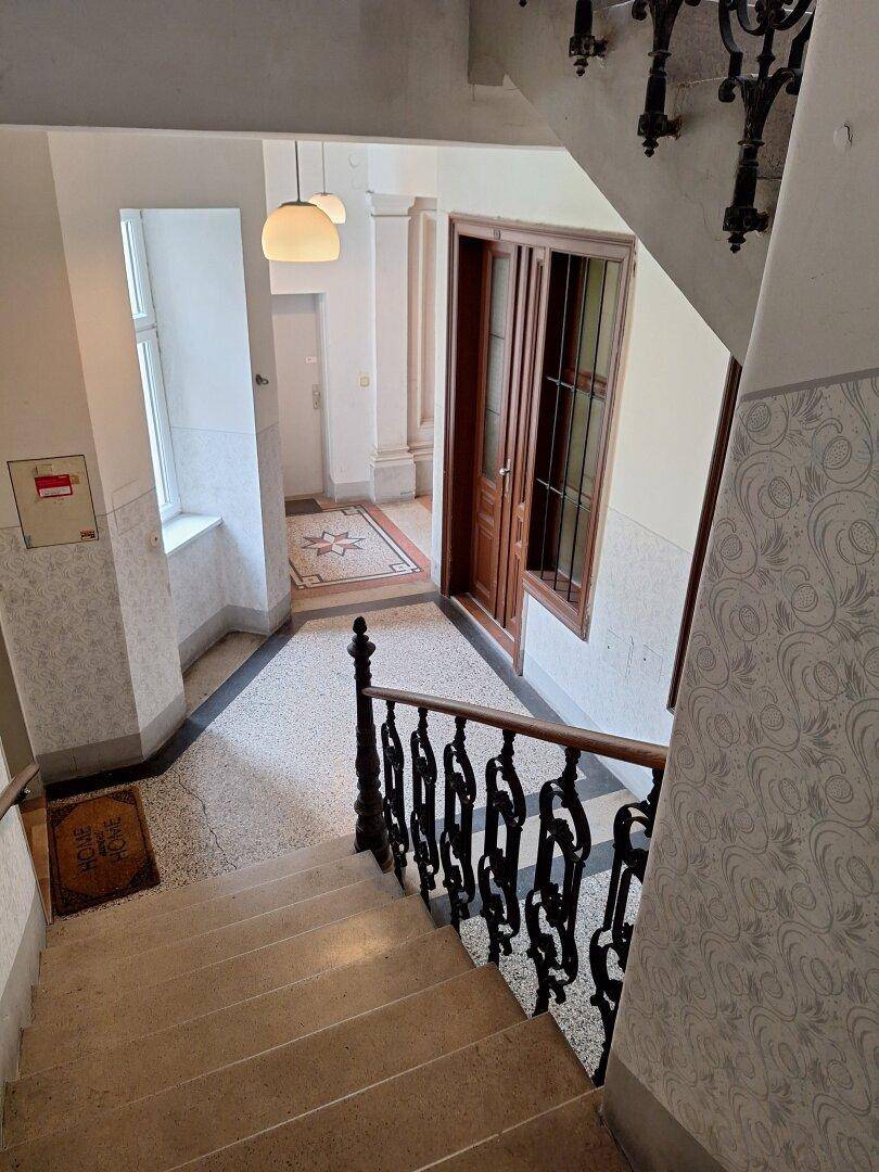 Historisches Treppenhaus mit Terrazzoboden, schmiedeeisernem Geländer und hohen Decken.