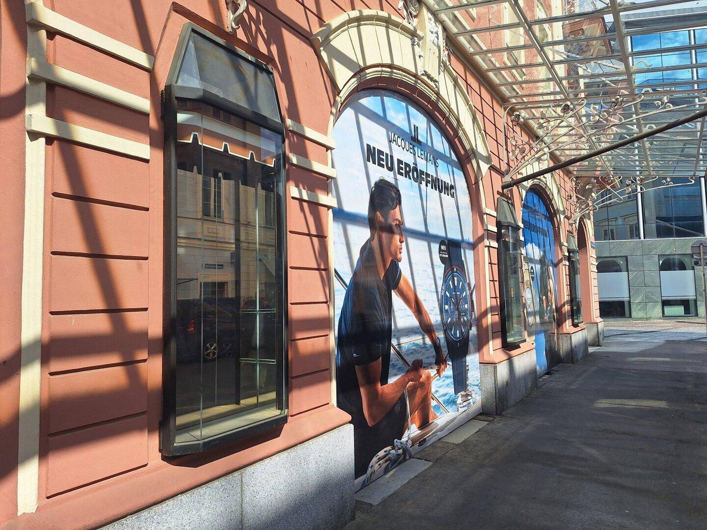 Detailansicht der Gebäudefassade mit einem großen Werbebanner in einem der Bogenfenster und seitlichen Schaufenstern.