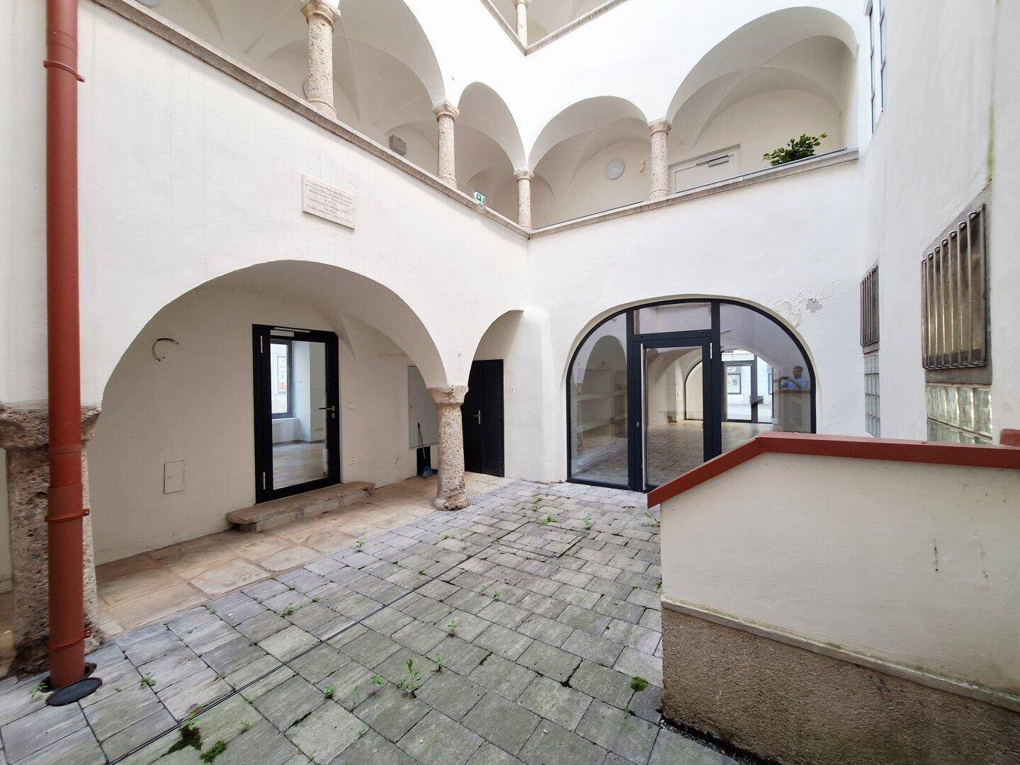 Historischer Innenhof mit Arkaden und Steinboden, der zu verschiedenen Eingängen führt.