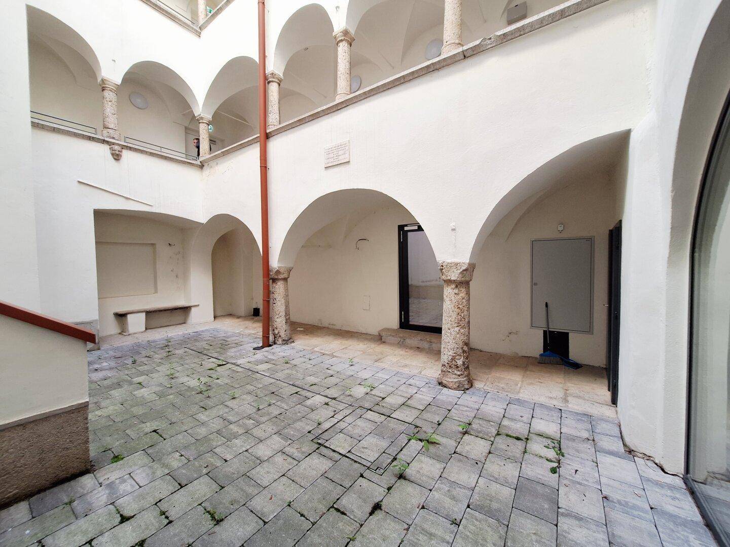 Weitläufiger Innenhof mit Arkadengängen und historischen Säulen, gepflastert mit Steinplatten.