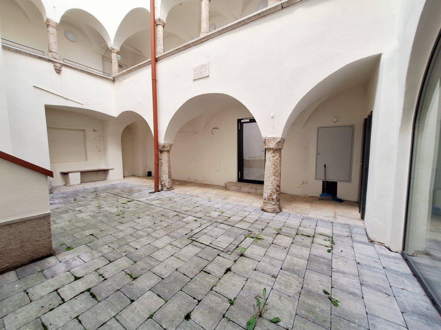 Historischer Innenhof mit Steinpflaster, Arkaden und Säulen, umgeben von weißen Wänden.