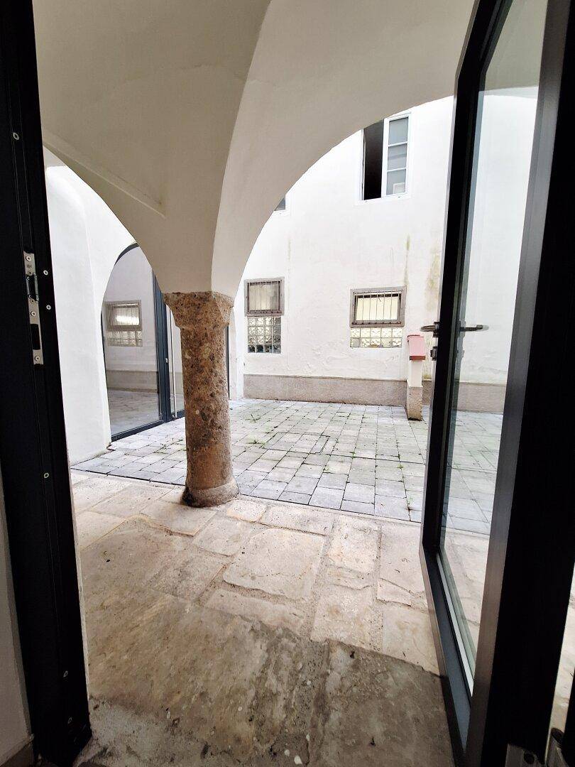 Blick durch eine offene Tür in einen historischen Innenhof mit Steinboden und Arkaden.