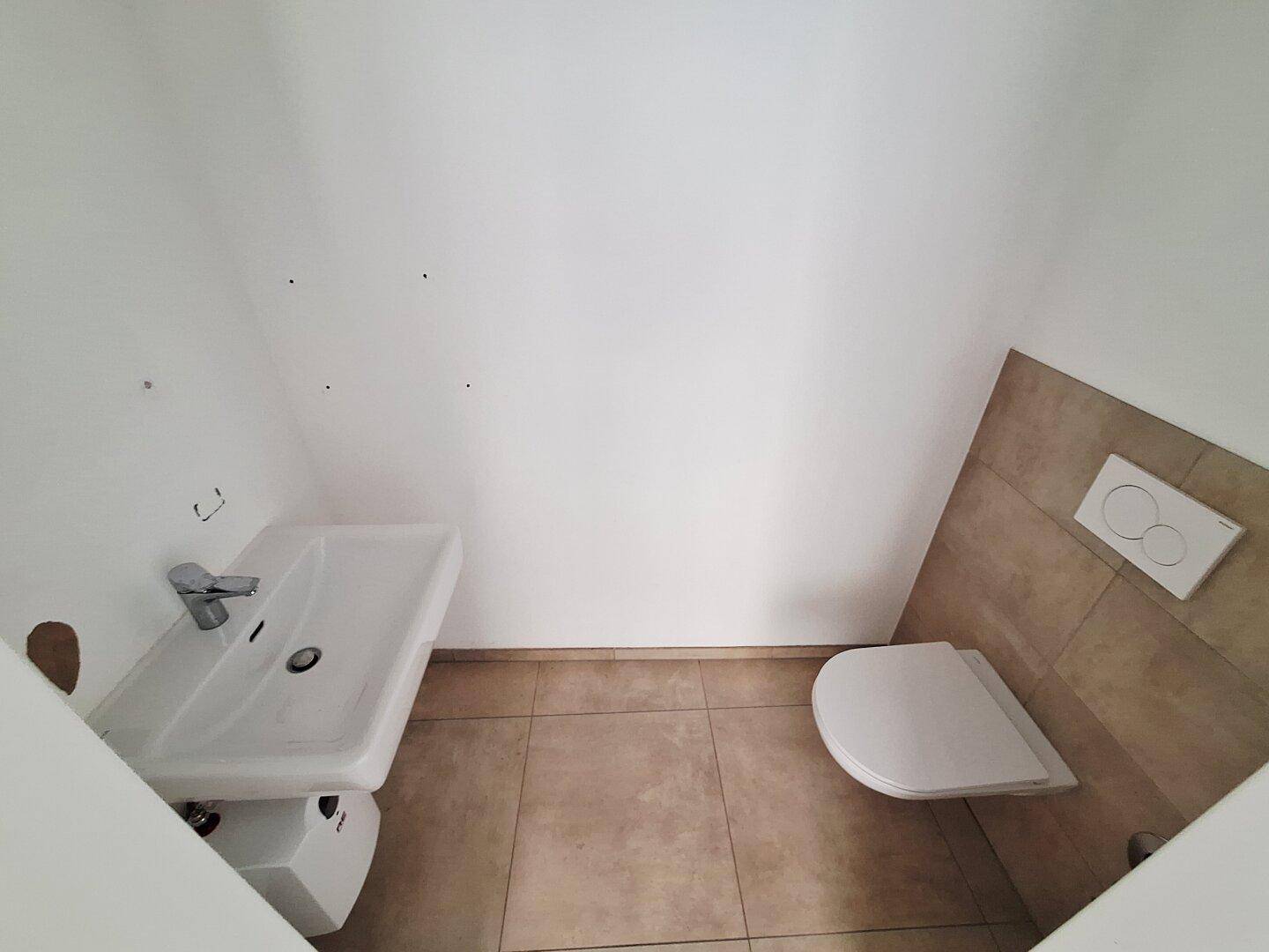 Modernes Gäste-WC mit wandhängender Toilette und Waschbecken, ausgestattet mit Fliesenboden.