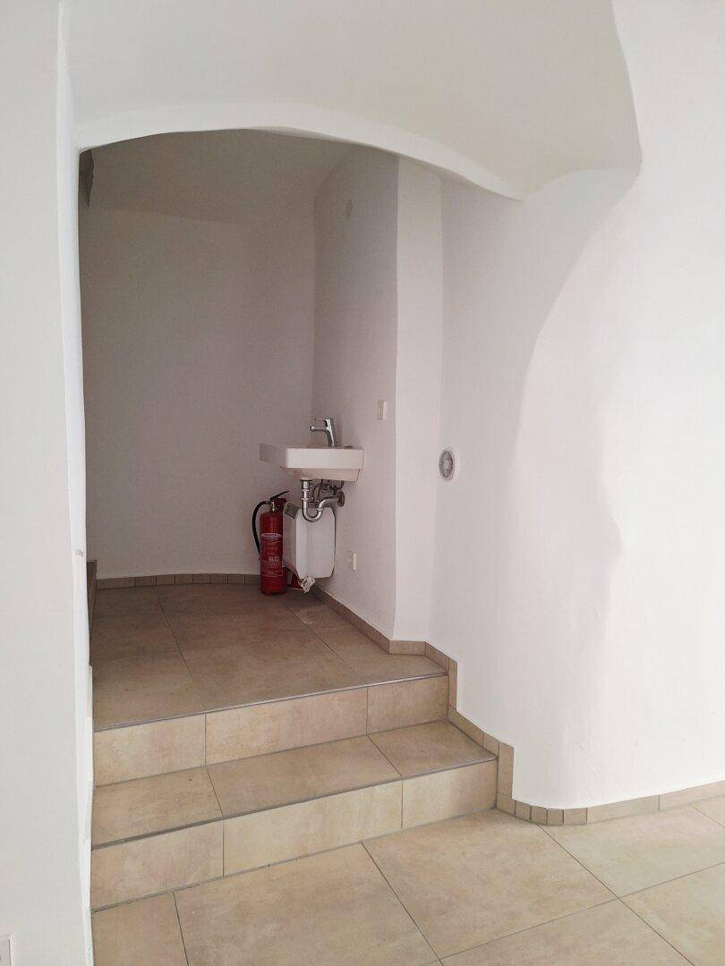 Kleiner Sanitärbereich mit Waschbecken und Feuerlöscher, zugänglich über eine kurze Treppe.