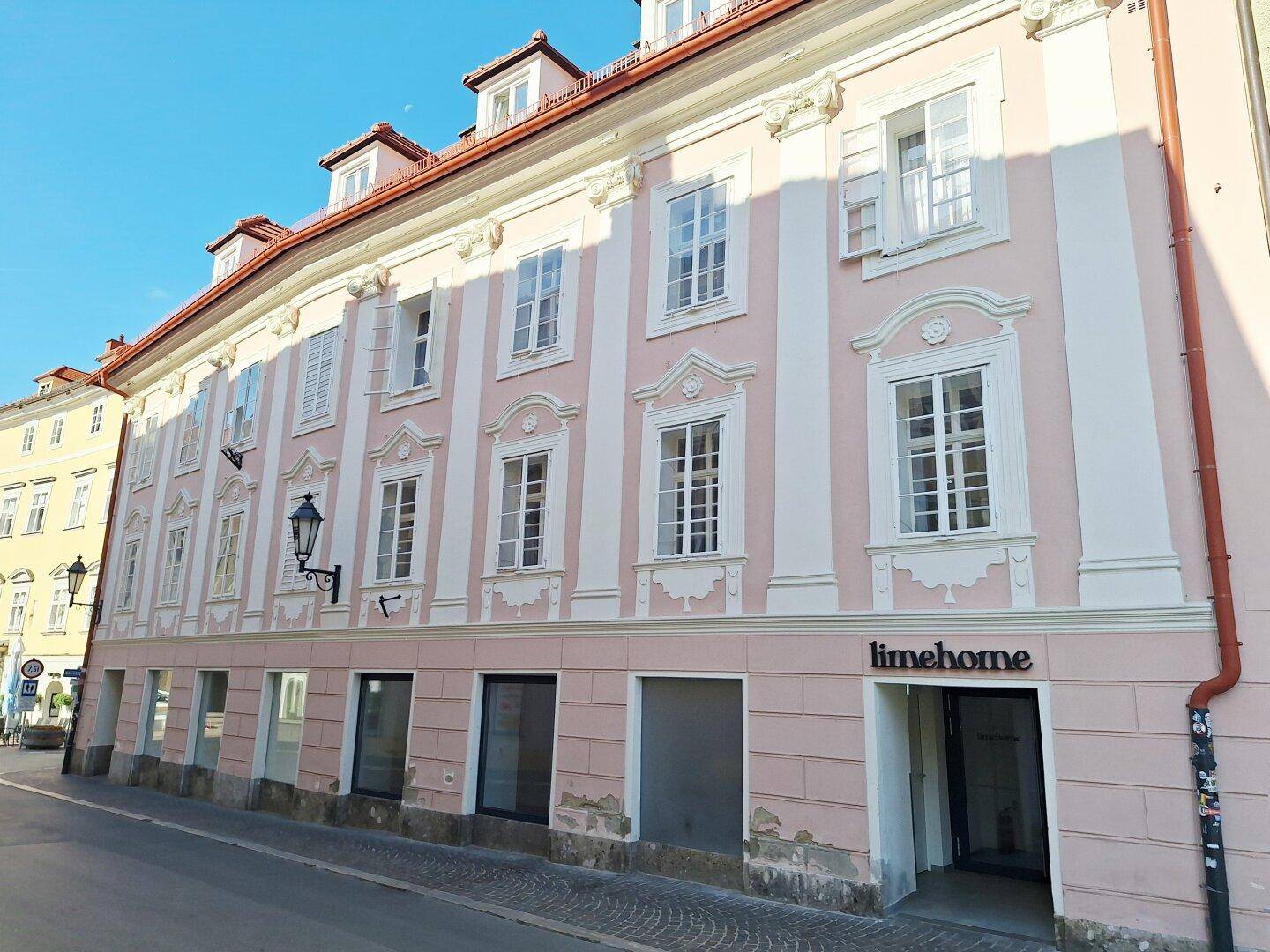 Lange Fassade eines historischen Gebäudes mit rosa Anstrich und vielen Fenstern.