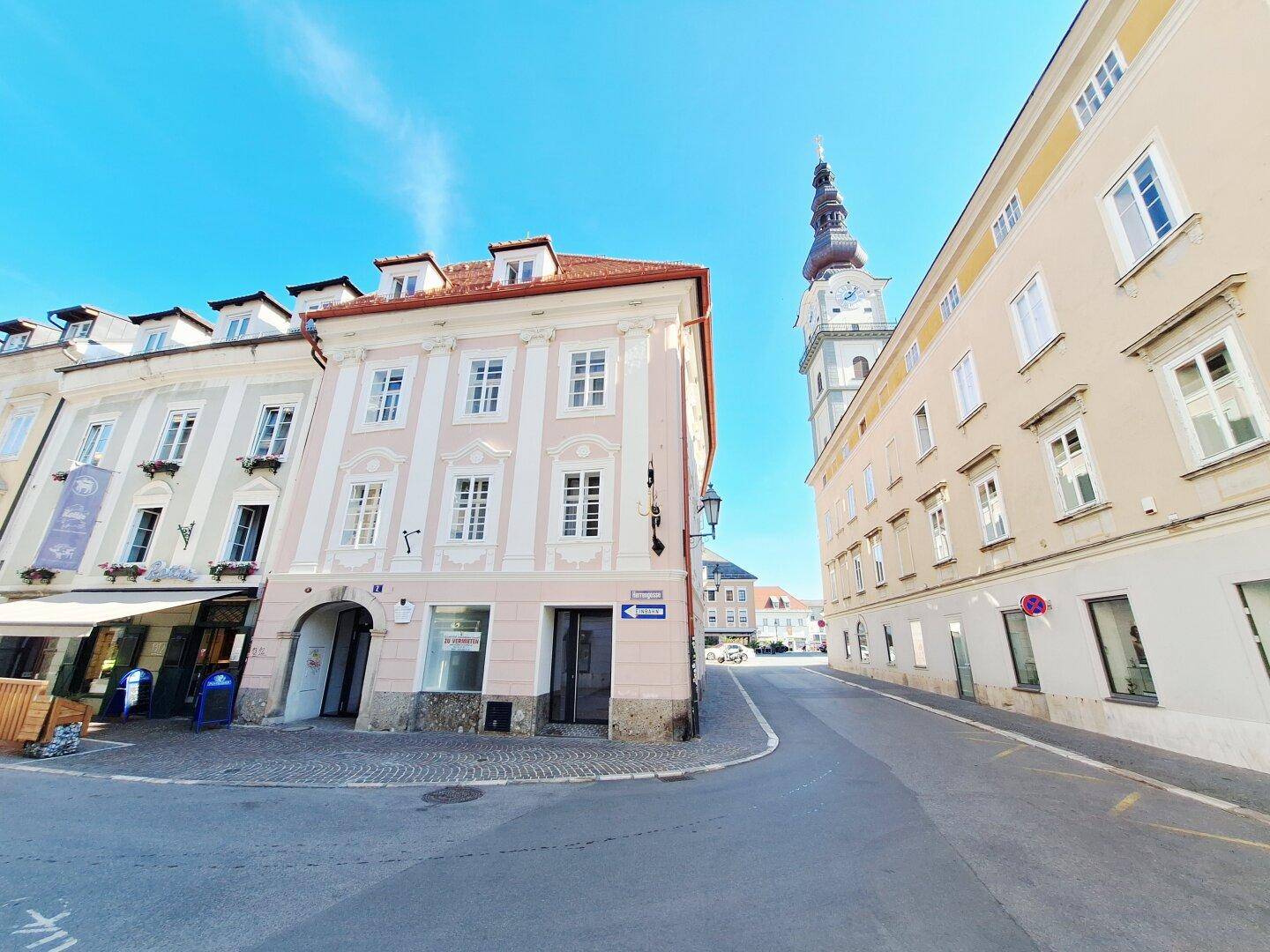 Historische Gebäudezeile mit rosa Fassade und einem prominenten Uhrturm im Stadtbild.