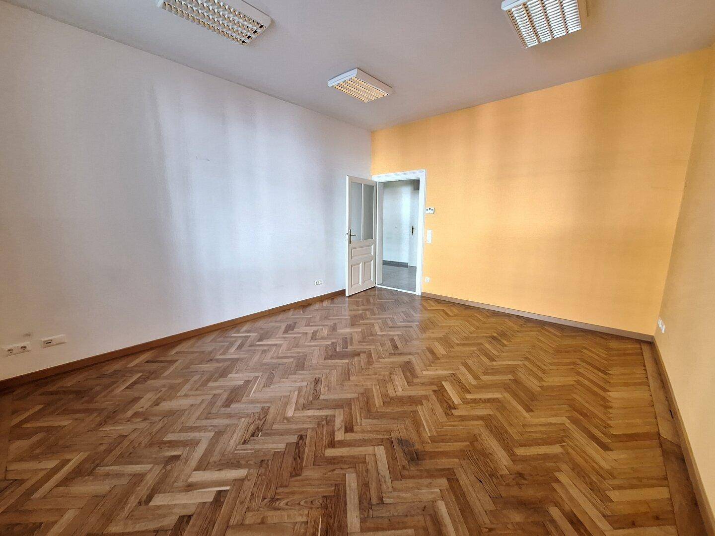 Heller Raum mit Fischgrätparkett, einer gelben Akzentwand und einer offenen Tür.