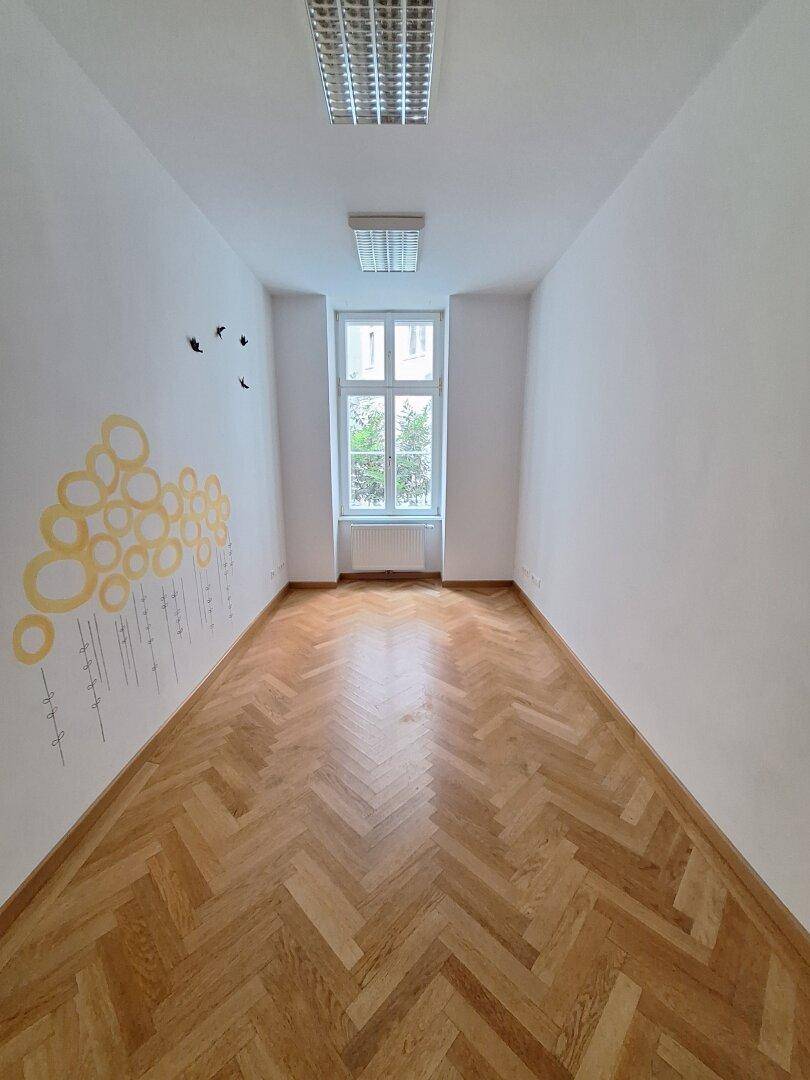 Langer, schmaler Raum mit Fischgrätparkett, gelben Wanddekorationen und einem Fenster am Ende.