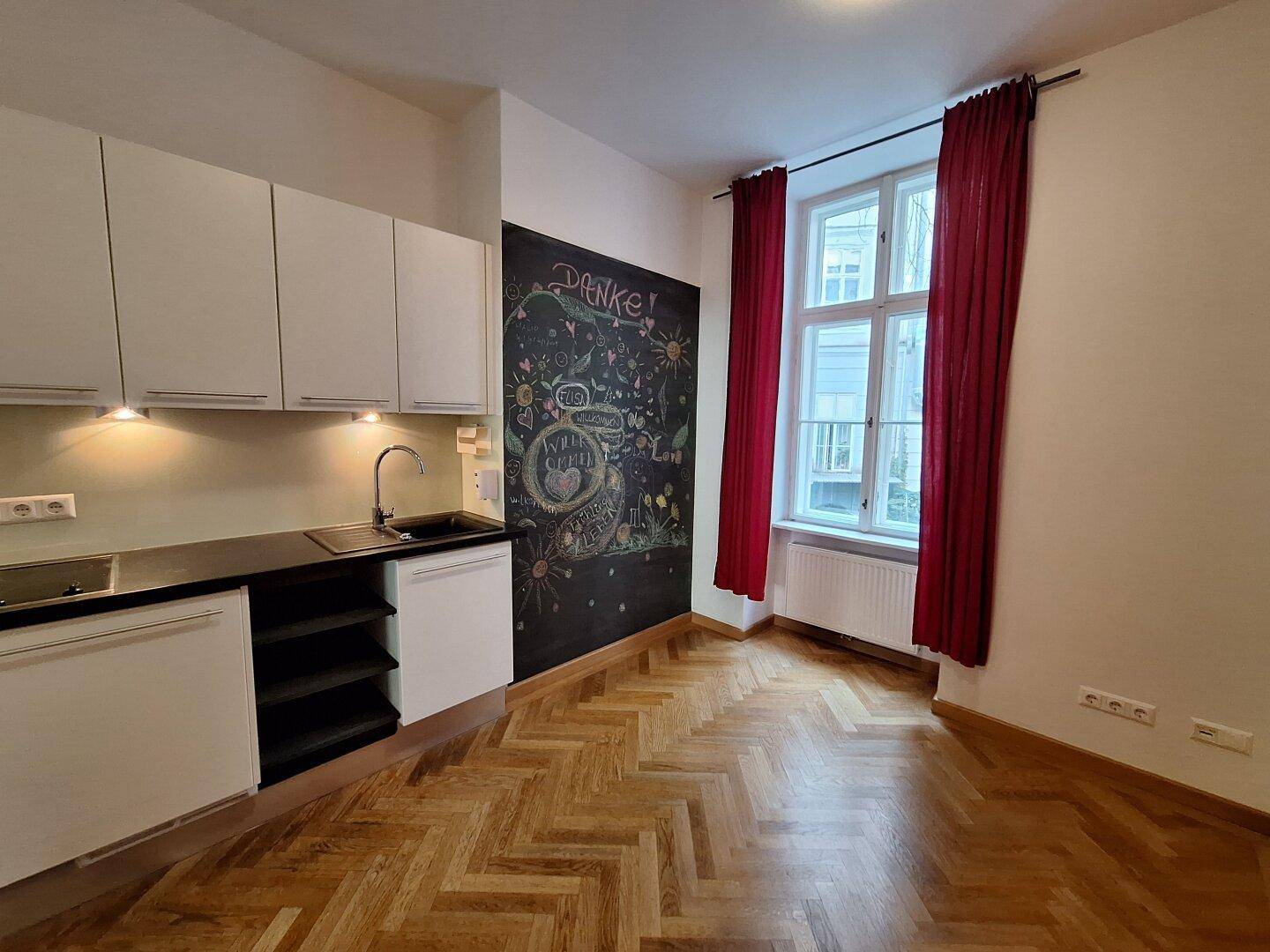 Kleine Küchenzeile mit weißen Schränken, schwarzer Arbeitsplatte und einer kreativen Kreidetafelwand.