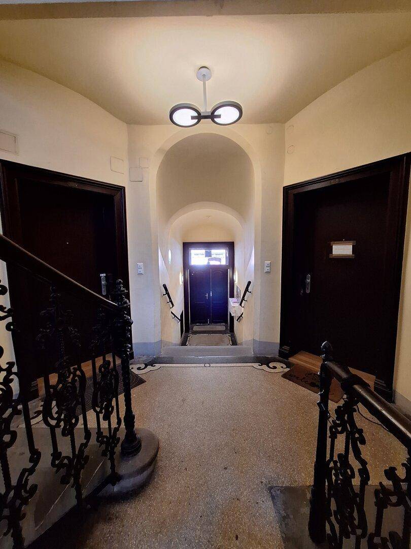 Historischer Eingangsbereich mit gewölbter Decke, dunklen Holztüren und einem verzierten Treppengeländer.