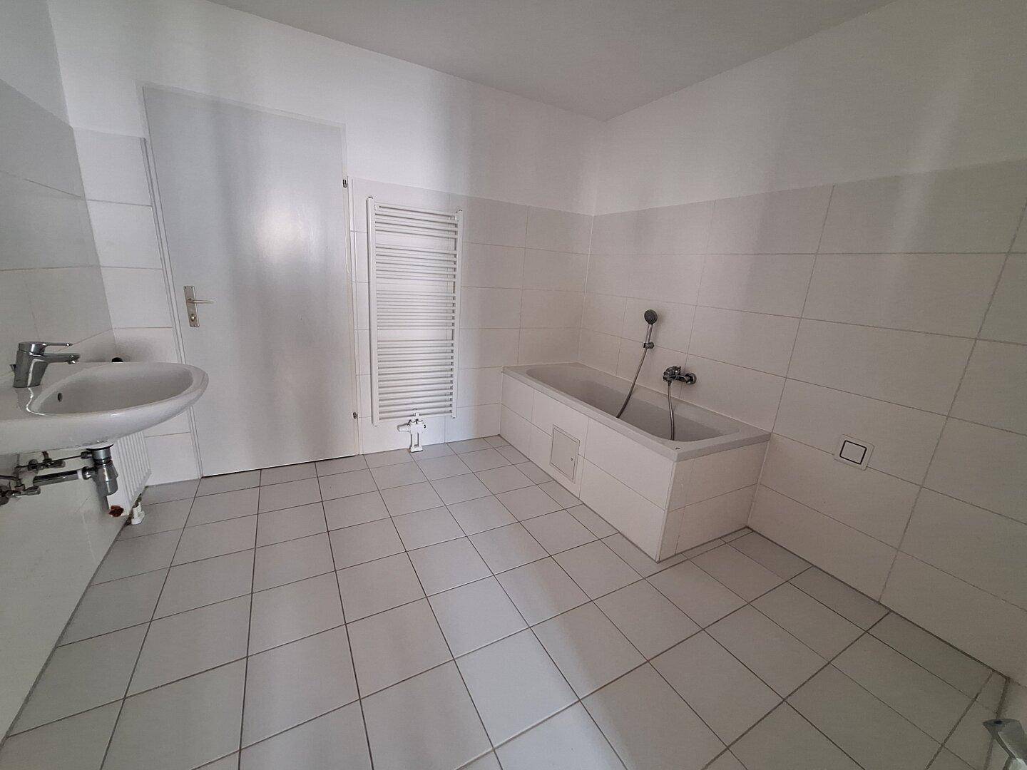 Helles Badezimmer mit weißen Fliesen, Badewanne und Waschbecken, ausgestattet mit Handtuchheizkörper.