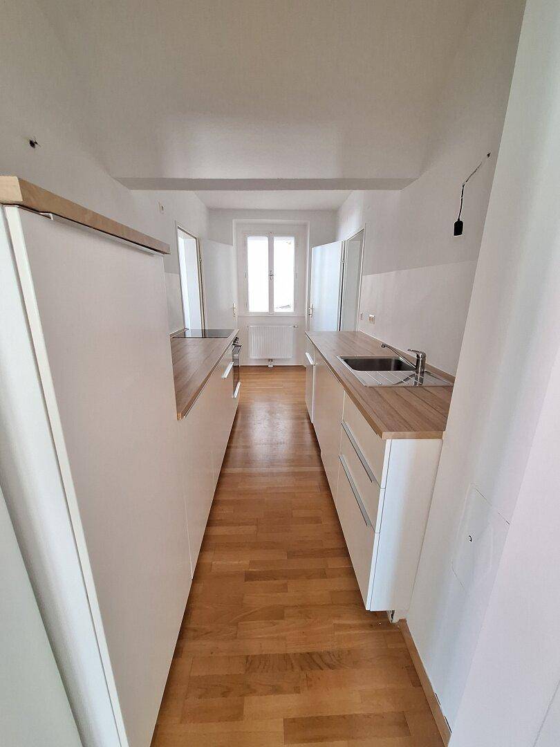 Moderne, schmale Küche mit weißen Schränken, Holzarbeitsplatten und integrierten Geräten.