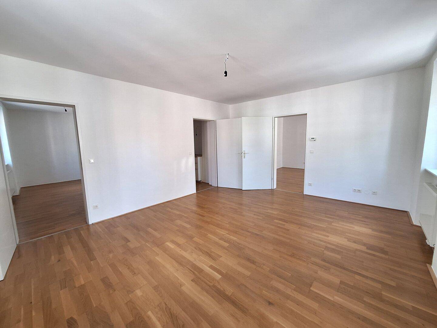 Geräumiges, leeres Zimmer mit Holzboden und mehreren Türen, das auf weitere Räume führt.