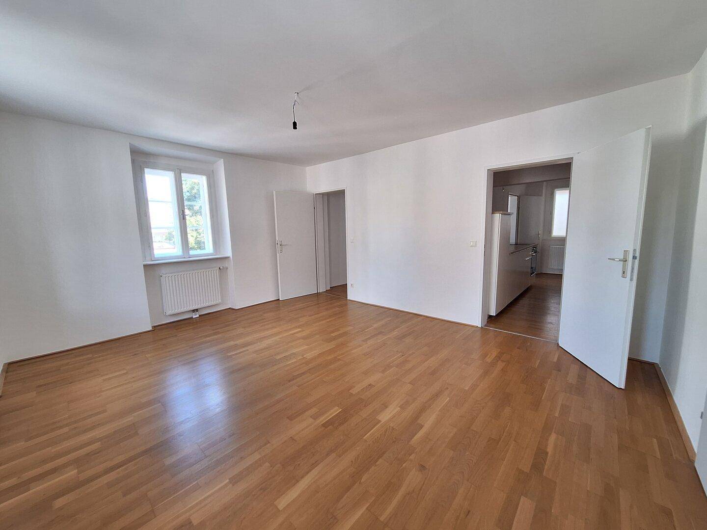Großes, helles Zimmer mit Parkettboden und Zugang zu einer Küche und weiteren Räumen.