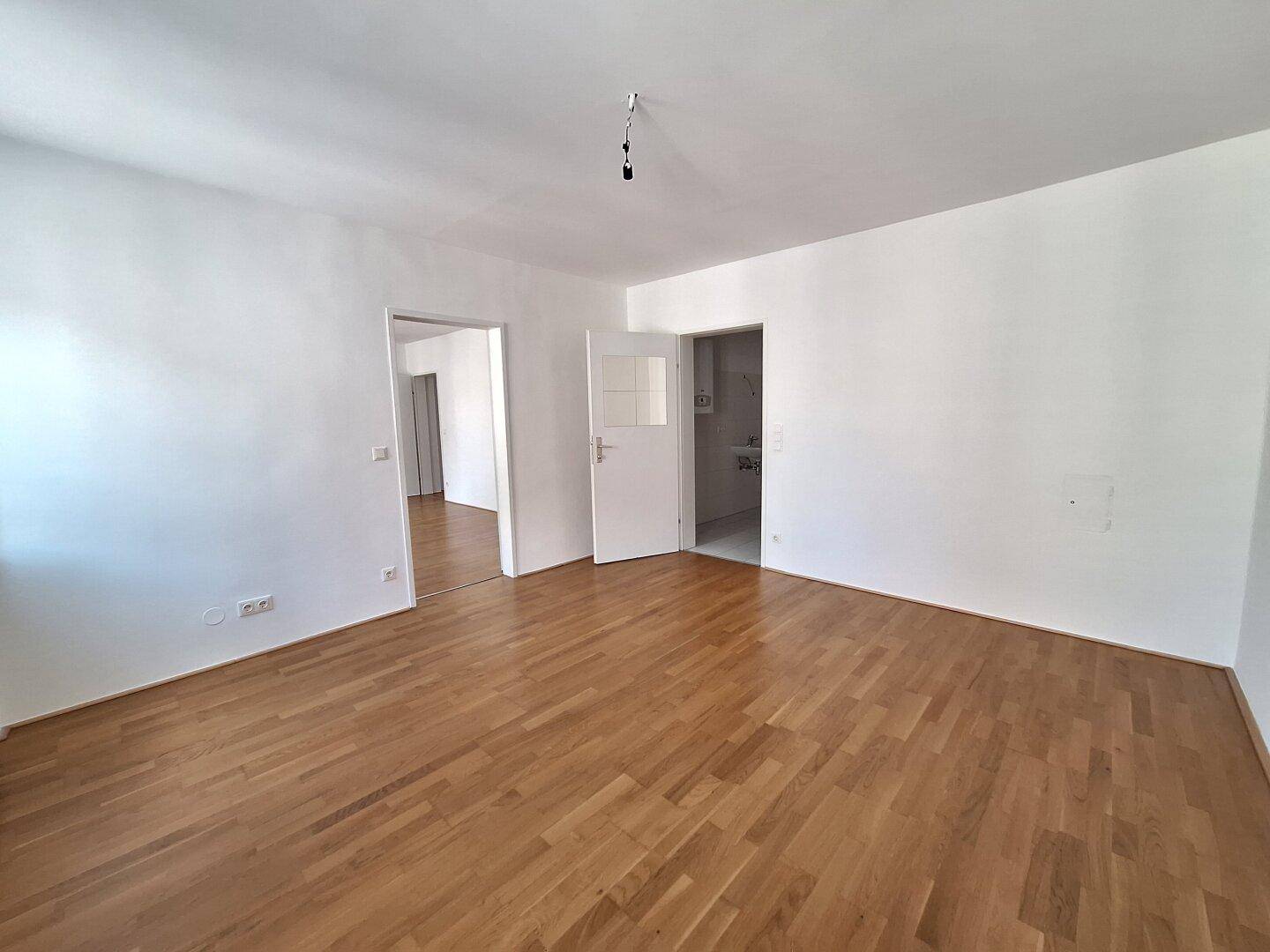 Geräumiges Zimmer mit Holzboden und Zugang zu einem Badezimmer und weiteren Räumen.