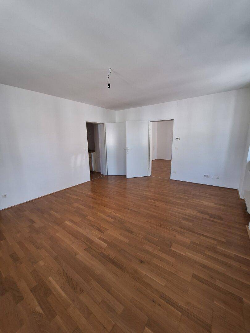 Geräumiges, leeres Zimmer mit Holzboden und mehreren Türen, das auf weitere Räume führt.