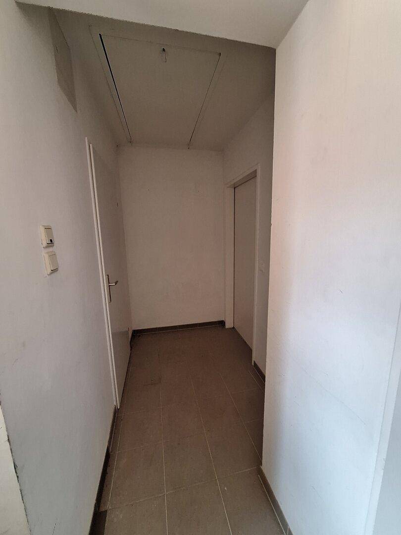 Schmaler Flur mit Fliesenboden und einer Dachluke, der zu einem weiteren Raum führt.