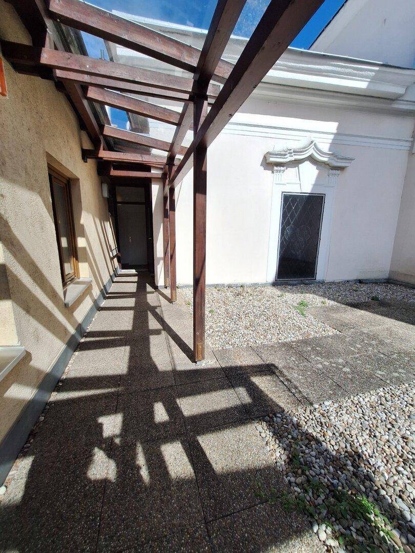Sonniger Außenbereich mit Kies und Steinplatten unter einer Holzpergola, ideal zum Entspannen.
