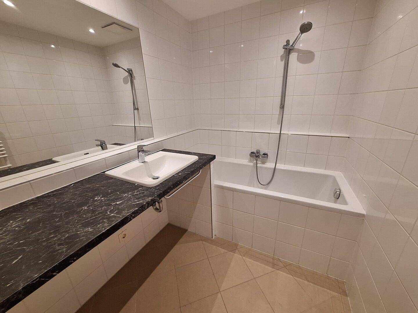 Badezimmer mit Badewanne, Duscharmatur, Waschbecken und großem Spiegel.
