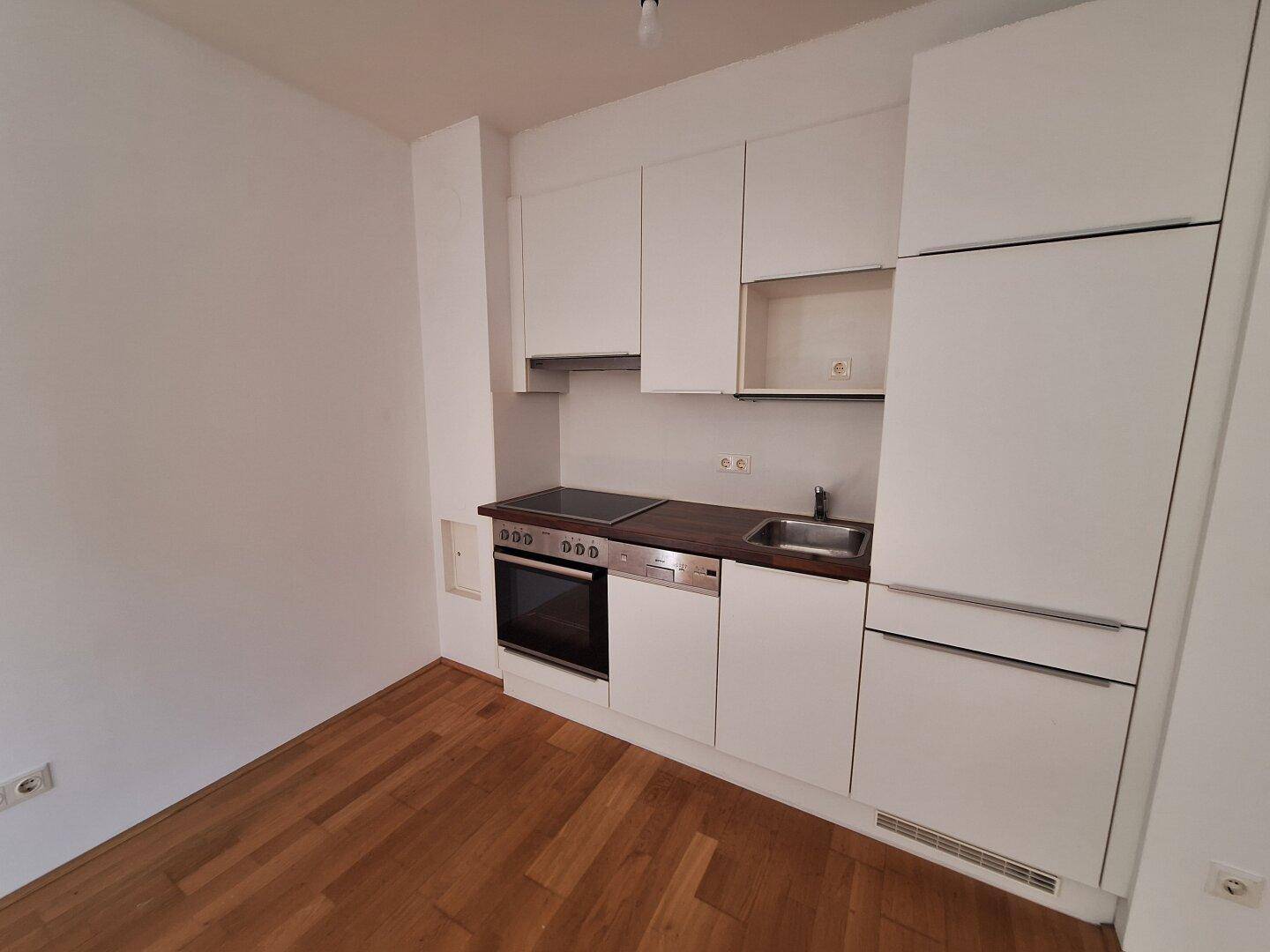 Moderne Küchenzeile mit weißen Schränken, Kochfeld, Backofen und Spülbecken.