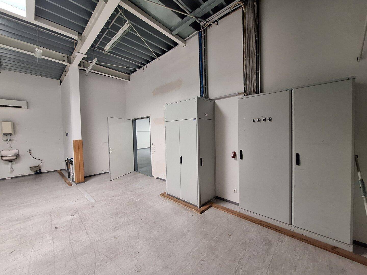 Großer, leerstehender Gewerberaum mit Betonboden, sichtbaren Deckenstrukturen und Elektroschränken.
