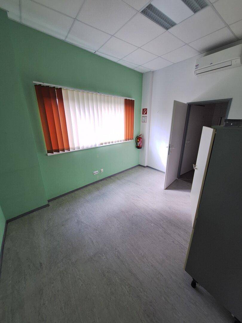 Kleines Büro mit hellgrünen Wänden, Fenster mit Jalousien und einer Klimaanlage für angenehmes Klima.