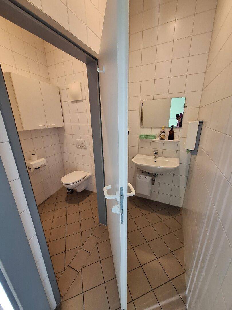 Badezimmer mit weißen Wandfliesen, grauem Boden, Waschbecken und einer modernen wandhängenden Toilette.