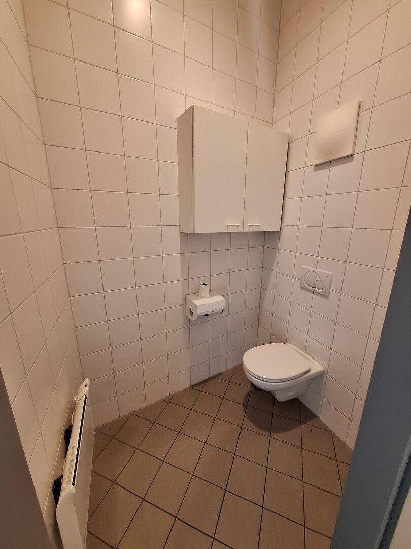 Kleine, geflieste Toilette mit Wand-WC, Spülkasten und einem Hängeschrank.