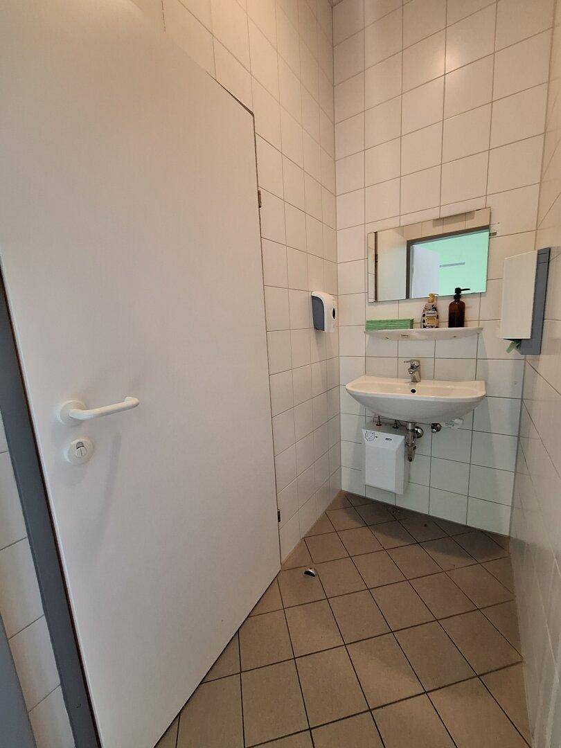 Badezimmer mit weißen Fliesen an Wänden und Boden, ausgestattet mit Waschbecken und Spiegel.