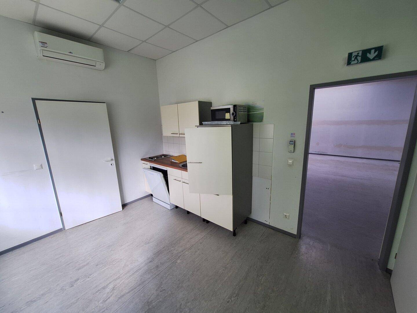 Küchenzeile mit Spüle, Kochfeld, Kühlschrank und Mikrowelle in einem Büroraum.