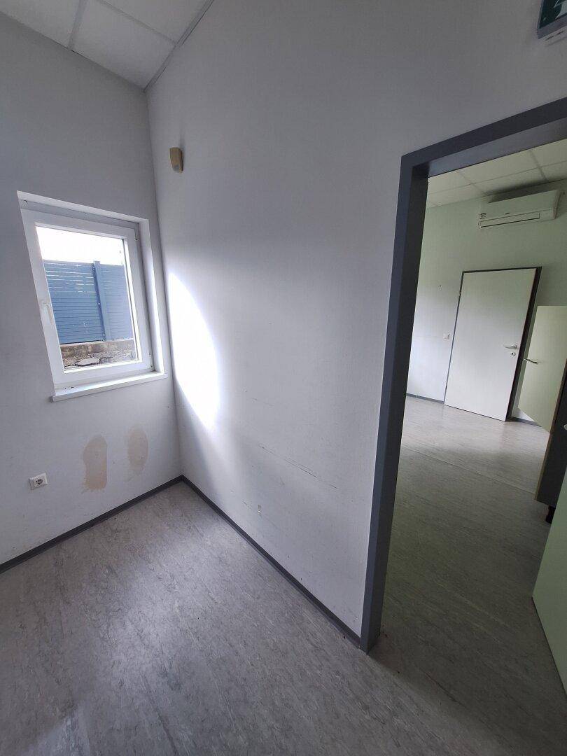 Helles kleines Büro mit weiß gestrichenen Wänden, einem Fenster und Zugang zu einem angrenzenden Raum.