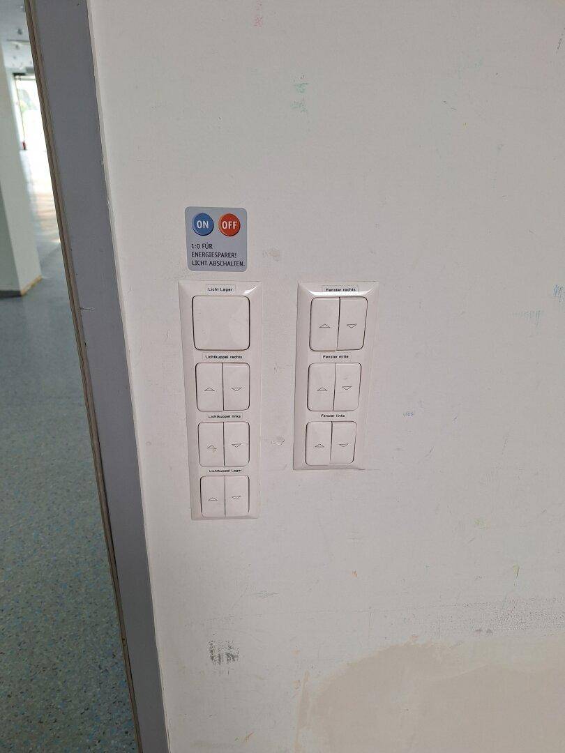 Wand mit mehreren Lichtschaltern und Hinweisen zur Energieeinsparung in einem Flur.
