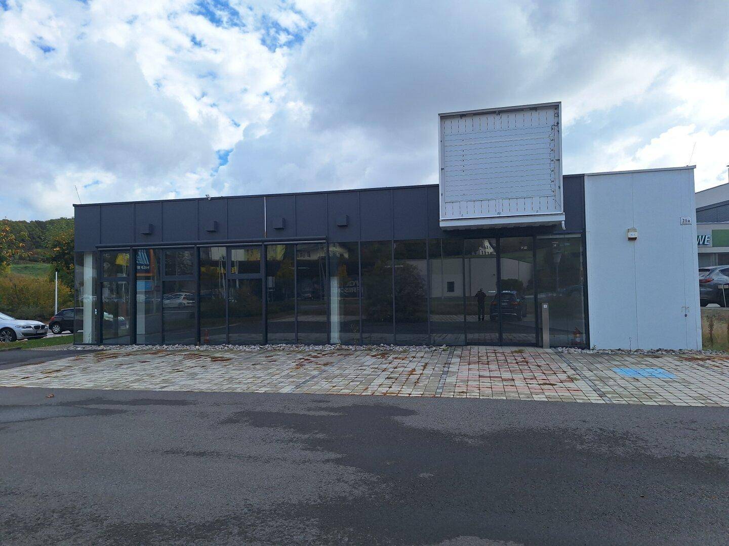 Gesamtansicht der modernen Geschäftsfassade mit großen Glasfenstern und einem geräumigen Parkplatz davor.