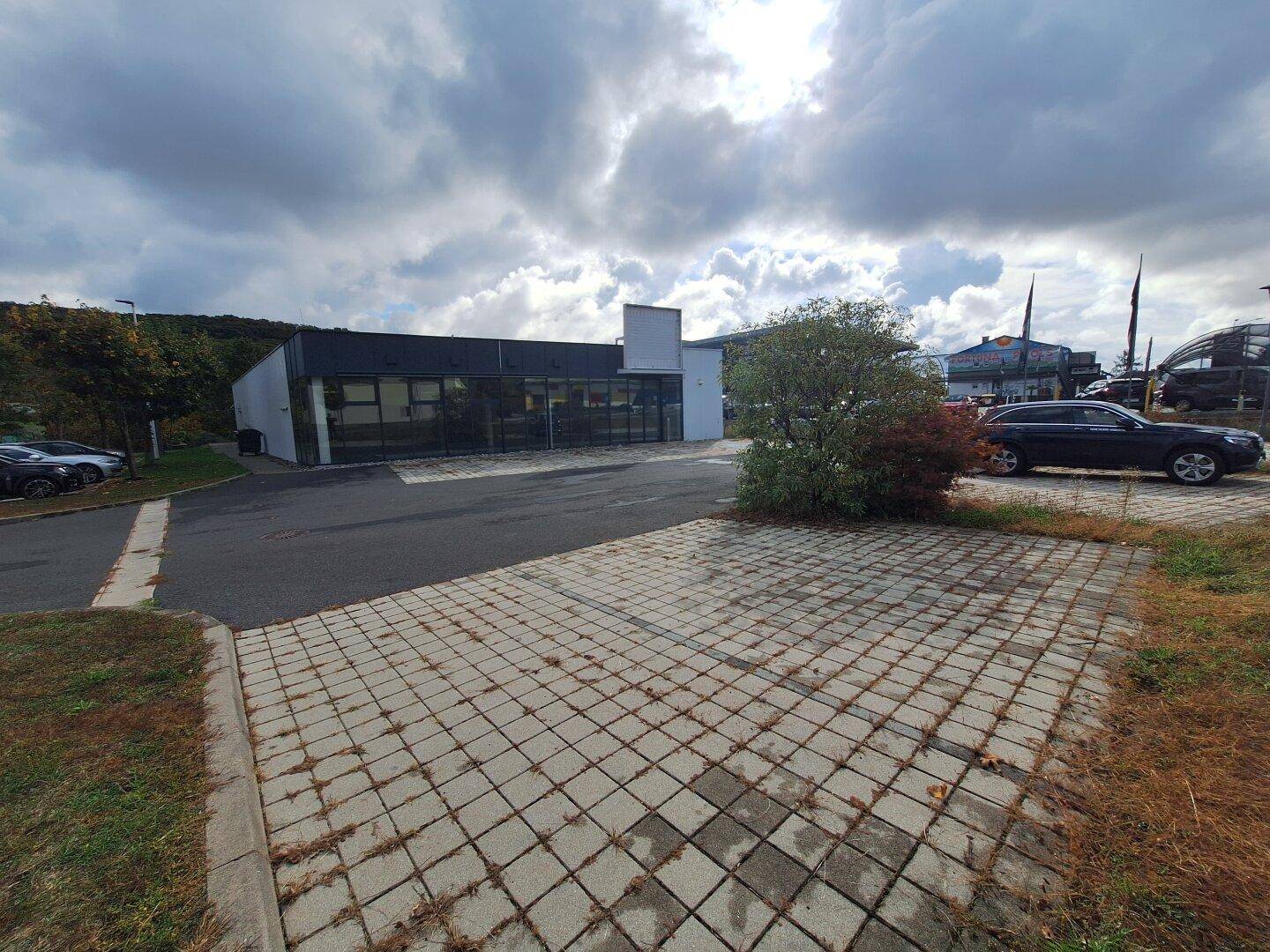 Weitläufiger Parkplatz vor einem modernen Geschäftsgebäude mit Glasfassade und bewölktem Himmel.