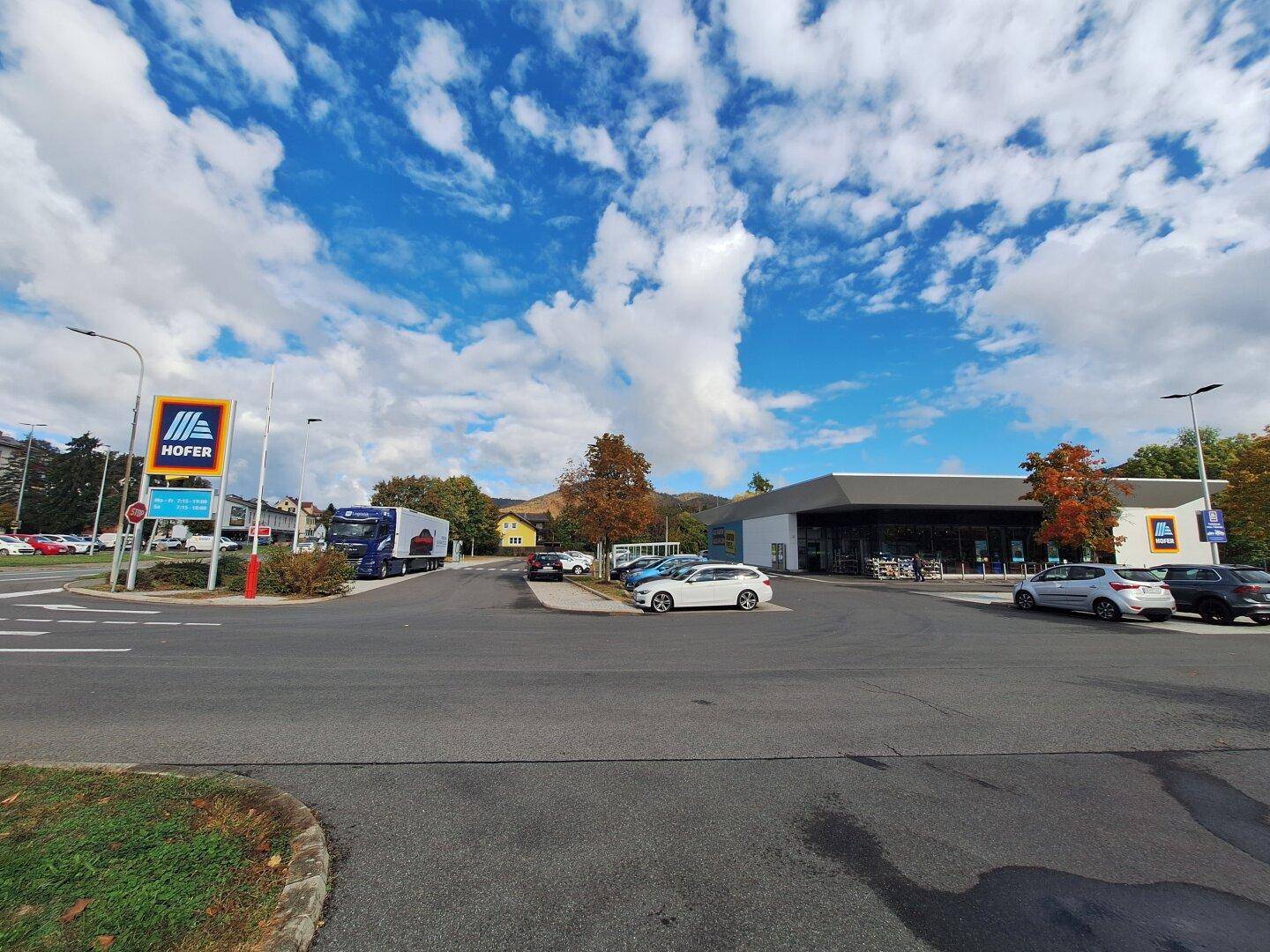 Außenansicht eines Supermarktes mit Parkplatz und einem Hofer-Schild unter blauem Himmel.