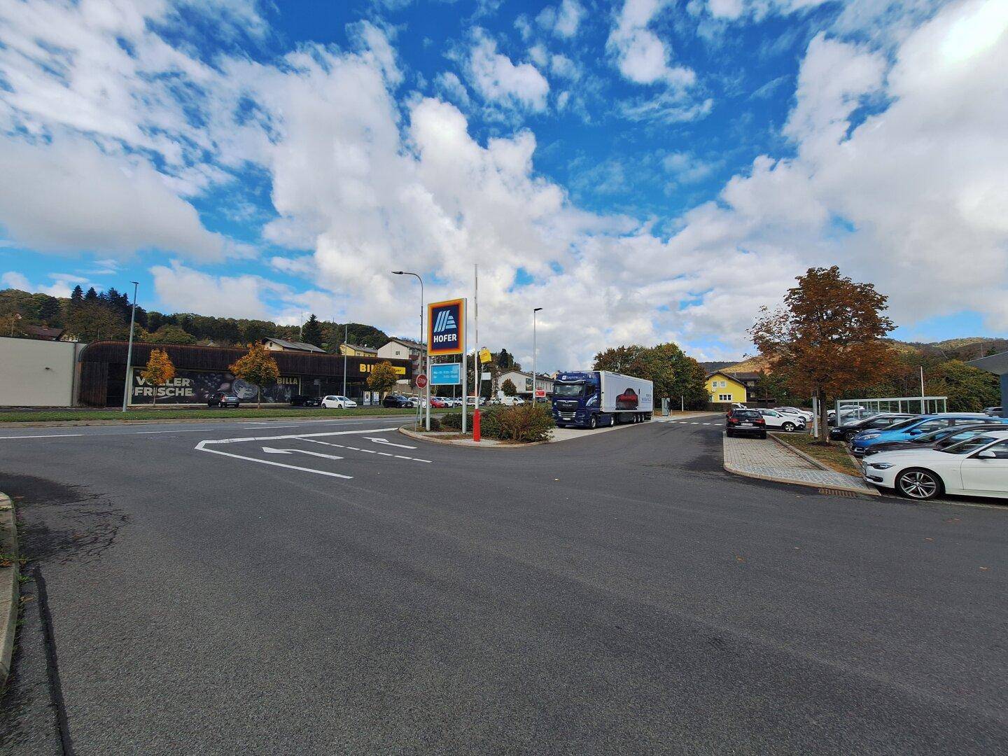 Kreuzung mit einem Hofer-Schild und einem Supermarkt im Hintergrund unter blauem Himmel.