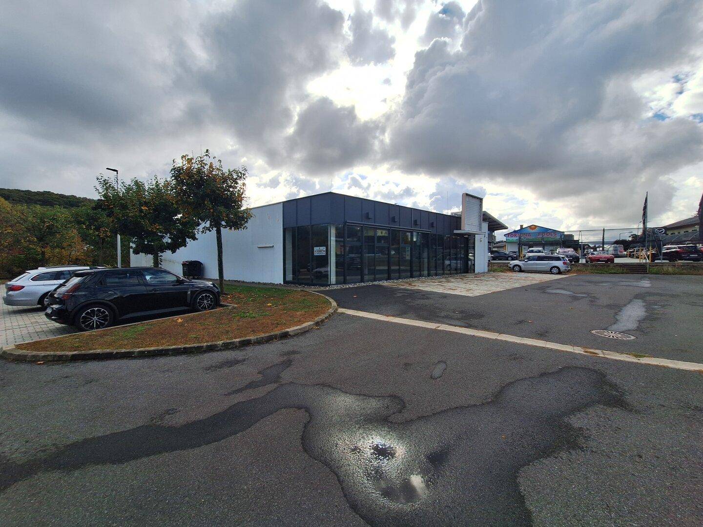 Parkplatz mit einem modernen Geschäftsgebäude im Hintergrund unter bewölktem Himmel.