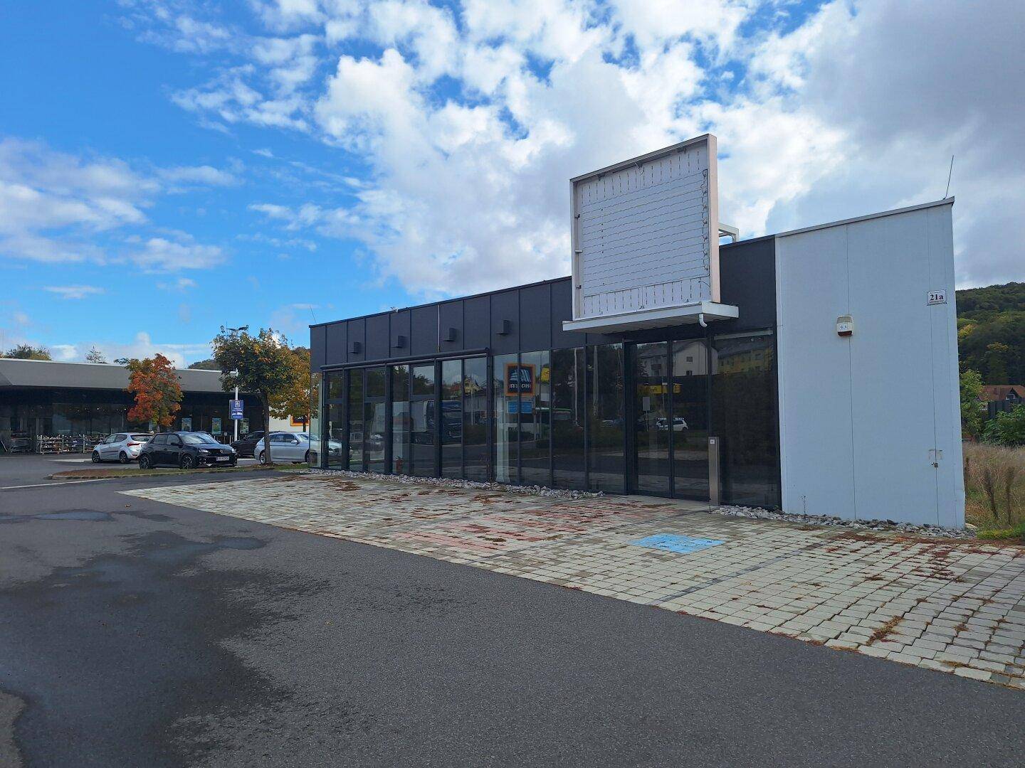 Modernes Geschäftsgebäude mit großer Glasfassade und einem leeren Werbeschild unter blauem Himmel.