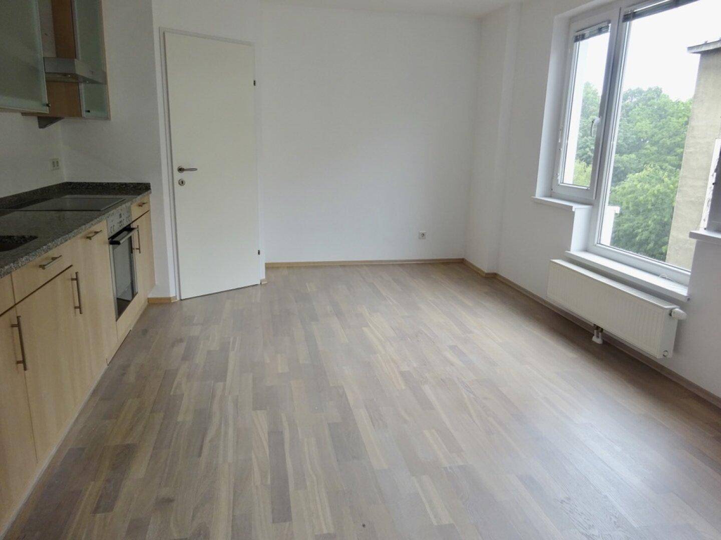Offene Küche mit hellen Holzschränken und Blick ins Grüne durch das Fenster.