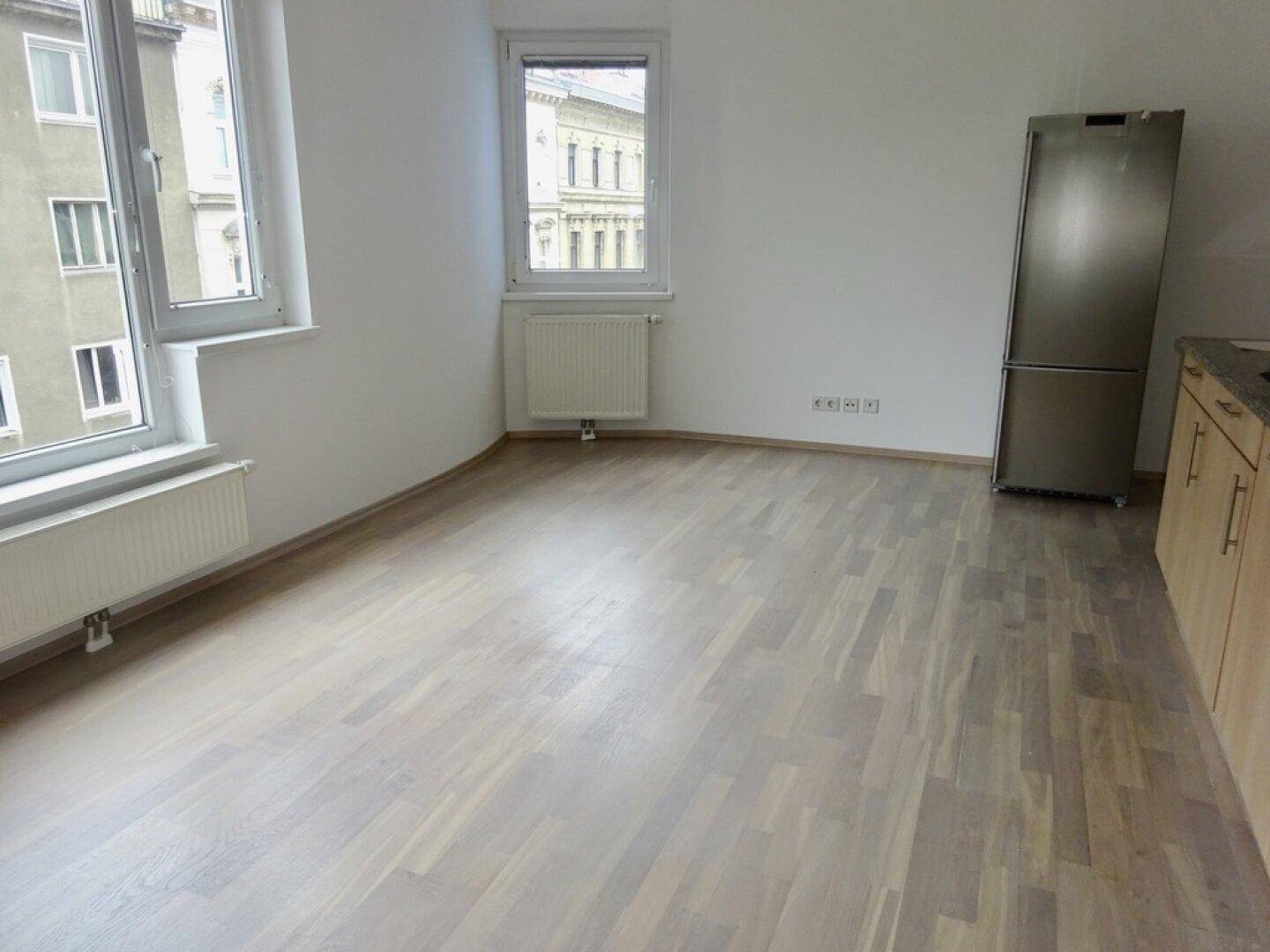 Heller Wohnbereich mit Parkettboden und großem Fenster, angrenzend an die Küche.