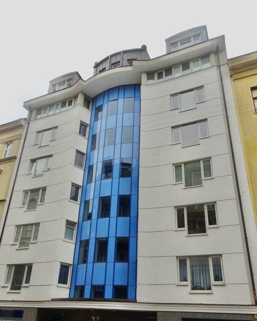Moderne Gebäudefassade mit blauer Glasfront und vielen Fenstern in urbaner Umgebung.
