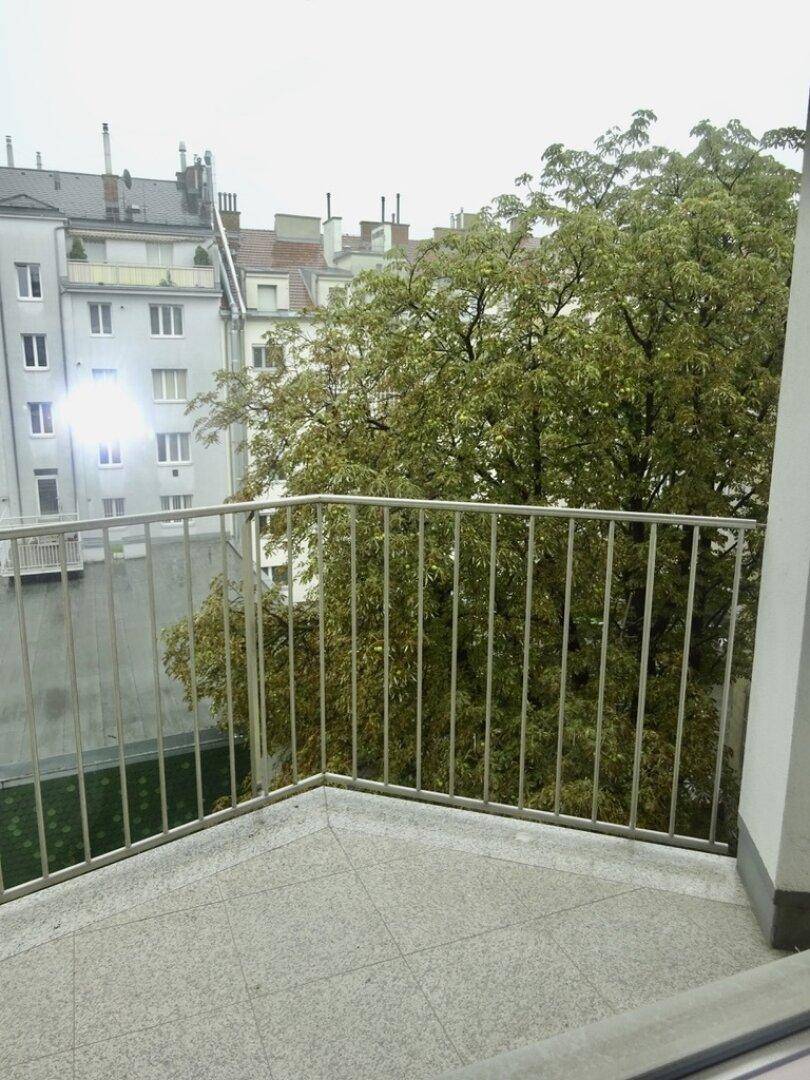 Kleiner Balkon mit Fliesenboden und Blick auf den begrünten Innenhof.