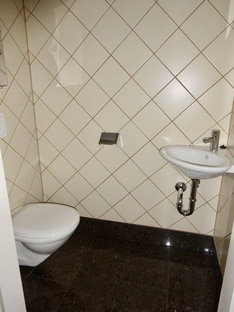 Kleines Gäste-WC mit Wand-WC, Waschbecken und diagonal verlegten Fliesen.