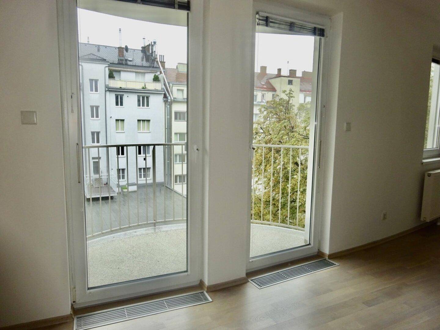 Blick aus dem Wohnzimmer auf den Balkon und den Innenhof mit umliegenden Gebäuden.