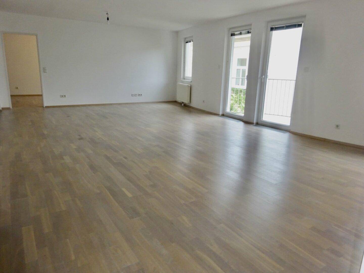 Helles Wohnzimmer mit Parkettboden und Zugang zu einem Balkon.