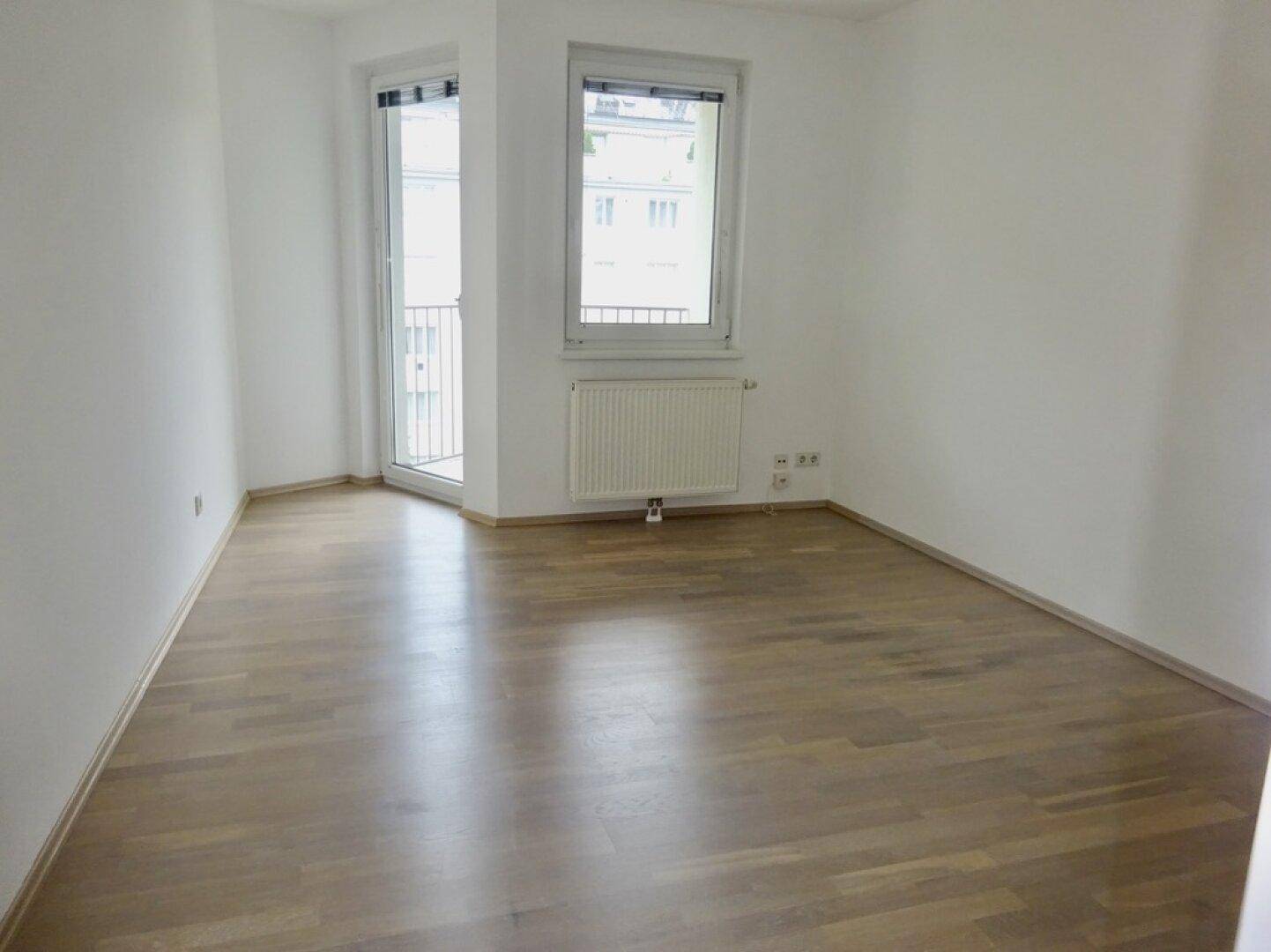 Helles Schlafzimmer mit Parkettboden und Zugang zu einem kleinen Balkon.
