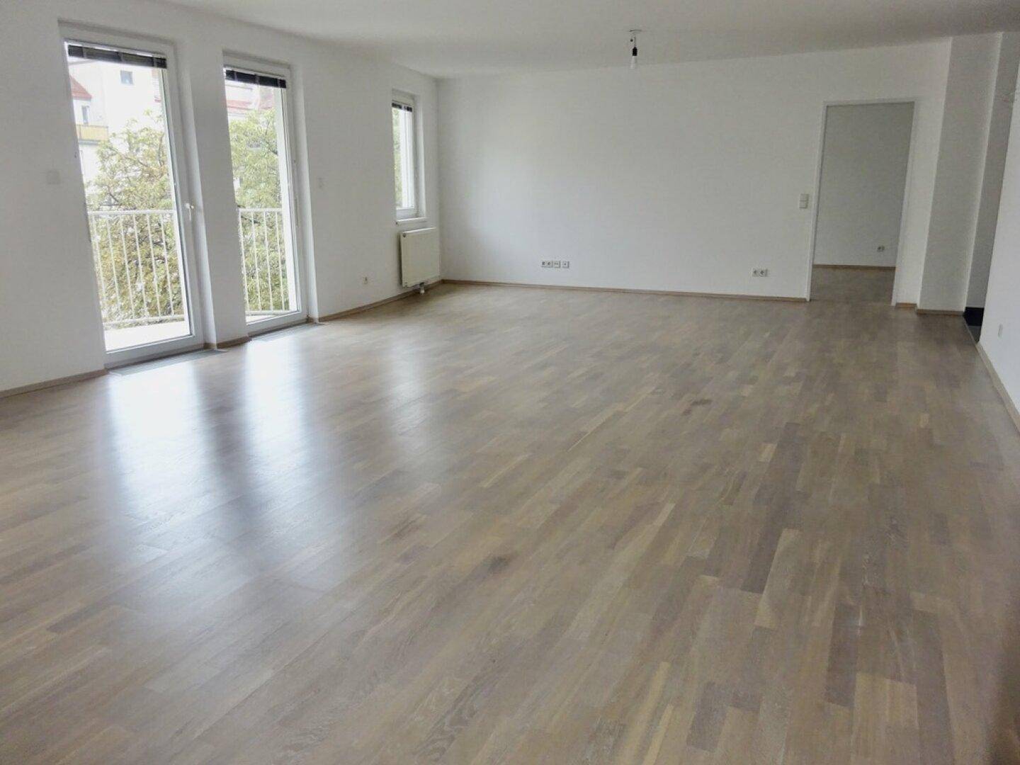 Geräumiges, helles Wohnzimmer mit Parkettboden und Zugang zu einem Balkon.