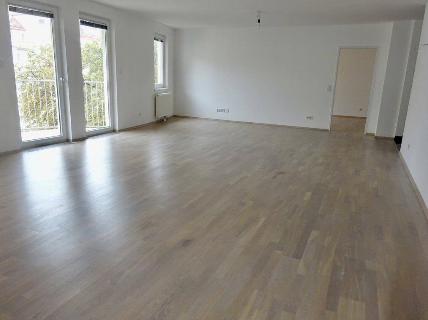 Geräumiges, helles Wohnzimmer mit Parkettboden und Zugang zu einem Balkon.