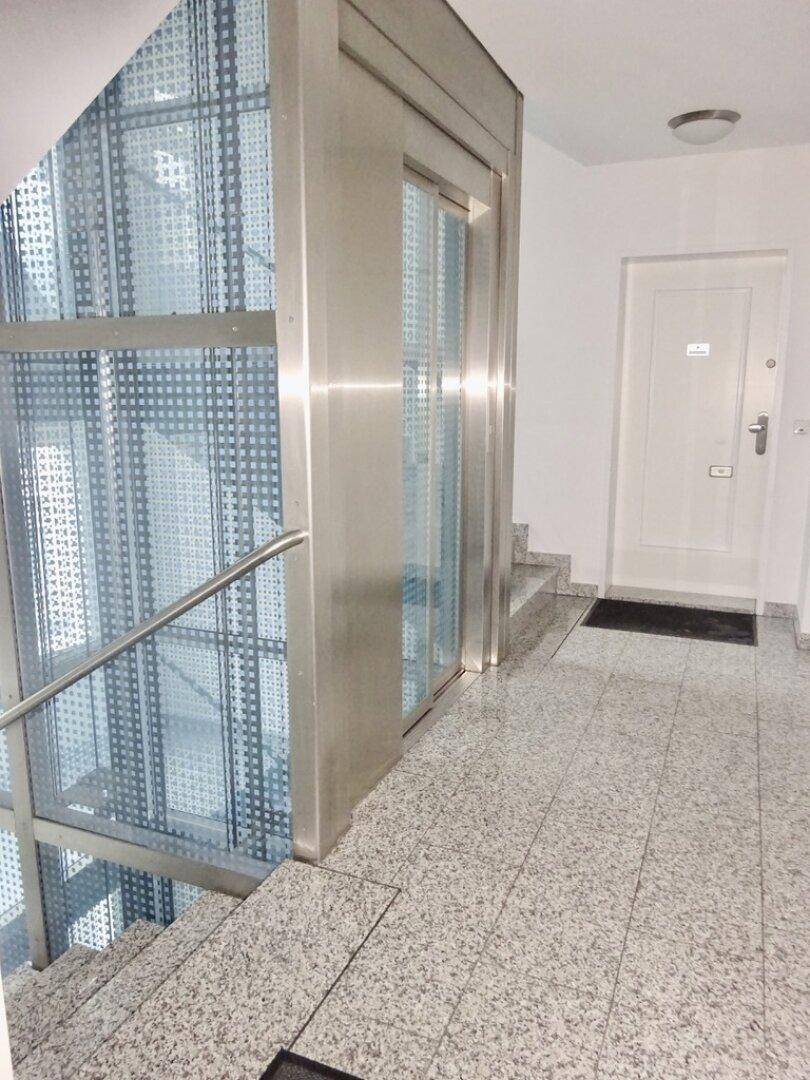 Eingangsbereich mit modernem Glasaufzug und Treppenhaus mit Granitfliesen.
